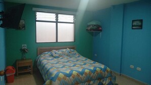 A bedroom with a bed, a window, a nightstand, a wall-mounted shelf, and a door.