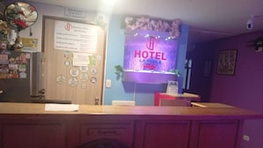 A hotel reception desk with a sign indicating room types, a mirror, and a wall-mounted sign with the hotel's name.