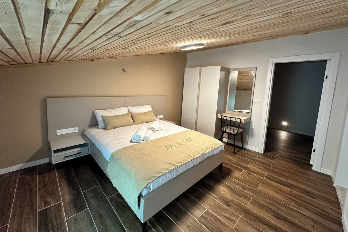 A bedroom with a bed, bedside table, wardrobe, mirror, and a small desk.