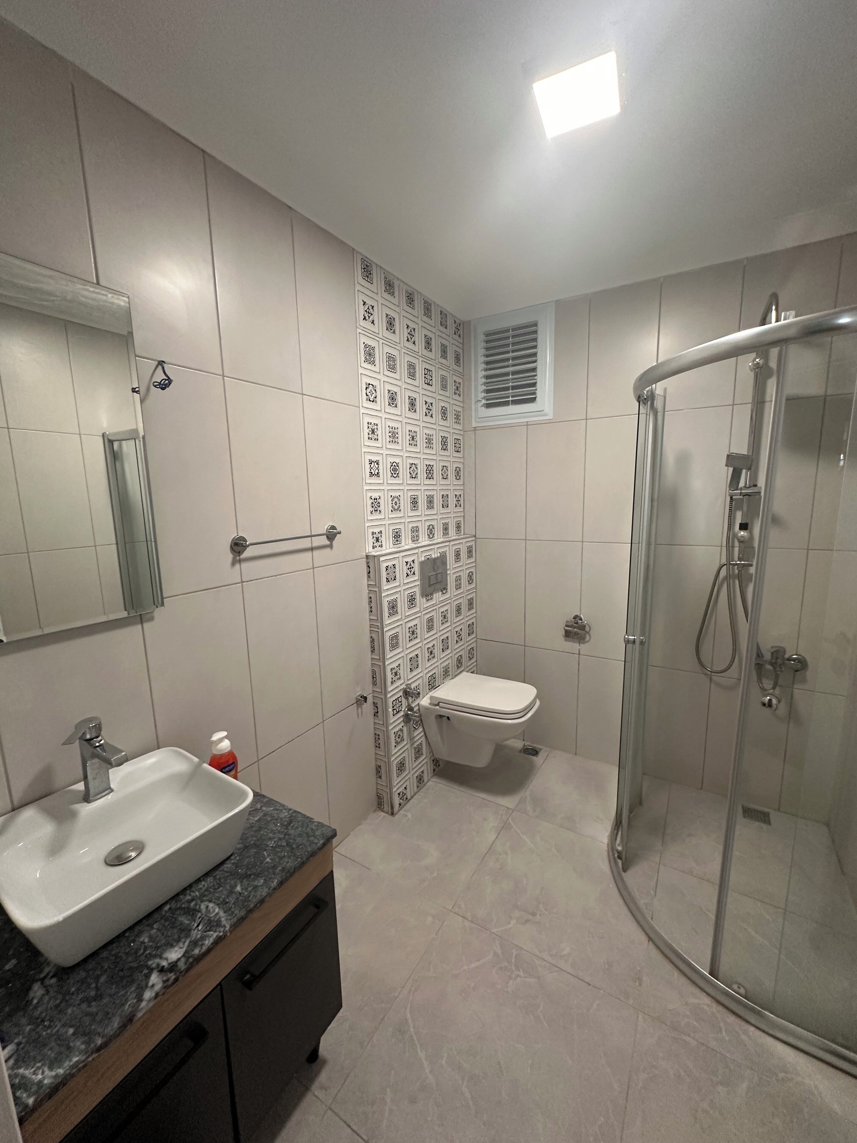 A bathroom with a sink, toilet, shower, and a mirror.