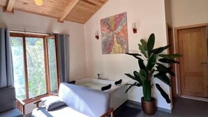 A room with a wooden ceiling, a large window, a bathtub, and a potted plant.