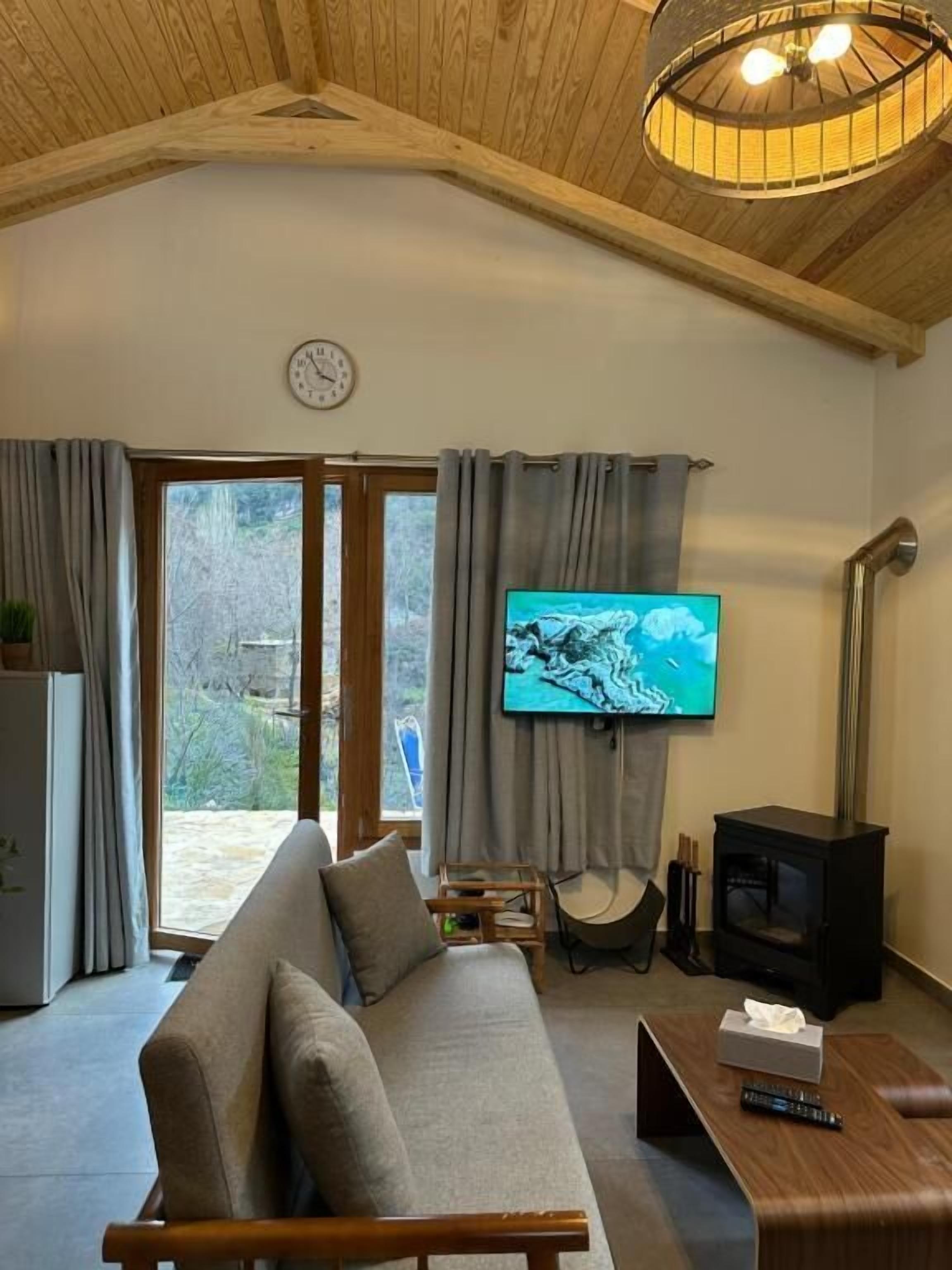 Un salon chaleureux avec un canapé, un téléviseur fixé au mur, un plafond en bois et une cheminée.