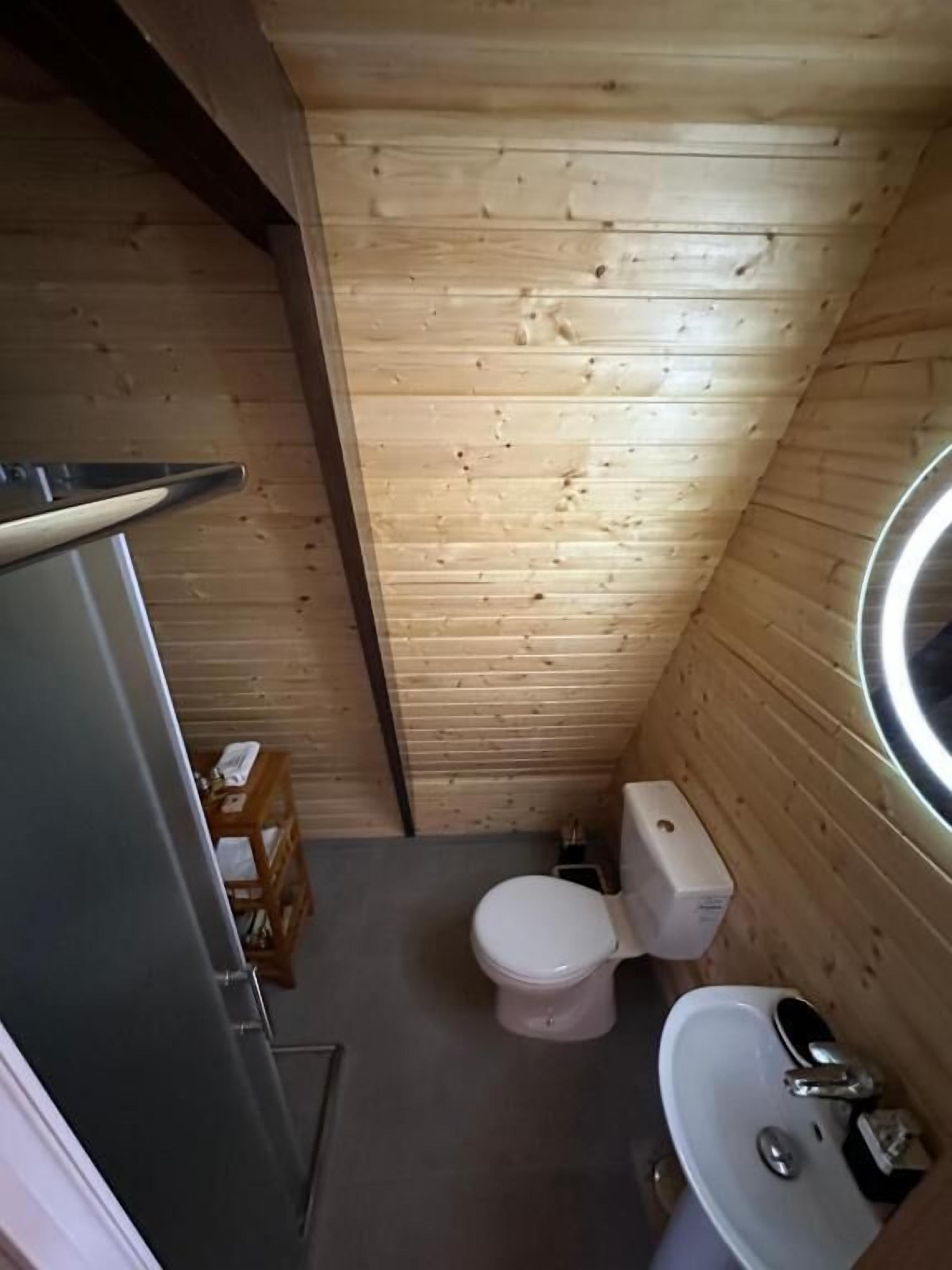 A small, wooden-paneled bathroom with a toilet, sink, and a mirror.