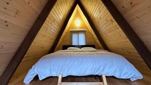 A triangular wooden room with a bed, a window, and a door.