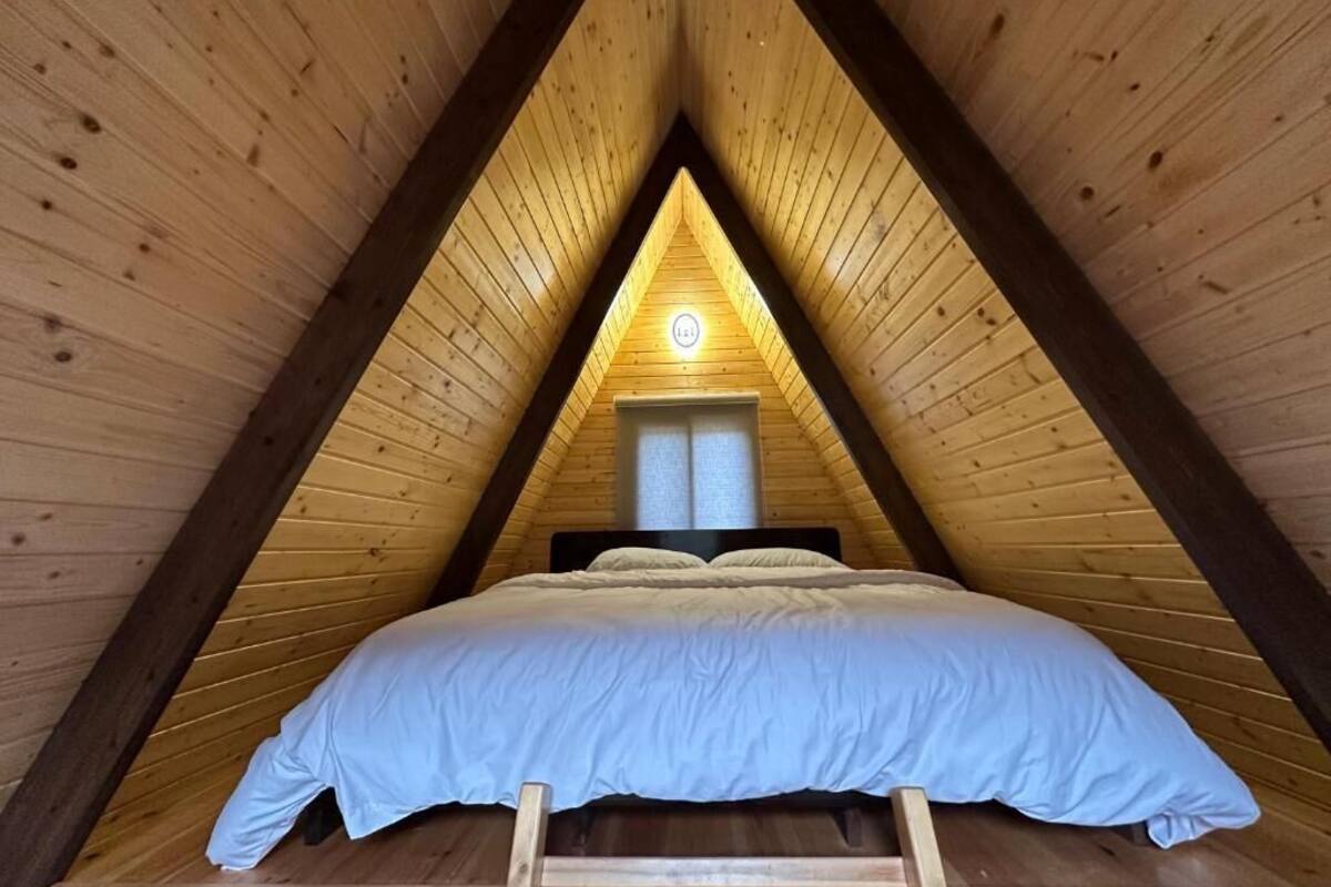 A triangular wooden room with a bed, a window, and a door.