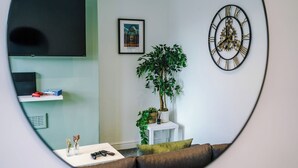 Una sala de estar con televisión, reloj, cuadro enmarcado, plantas en macetas y un sofá.