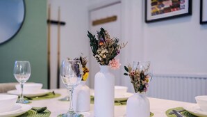 Una mesa de comedor con platos blancos, vasos transparentes y jarrones blancos con flores.