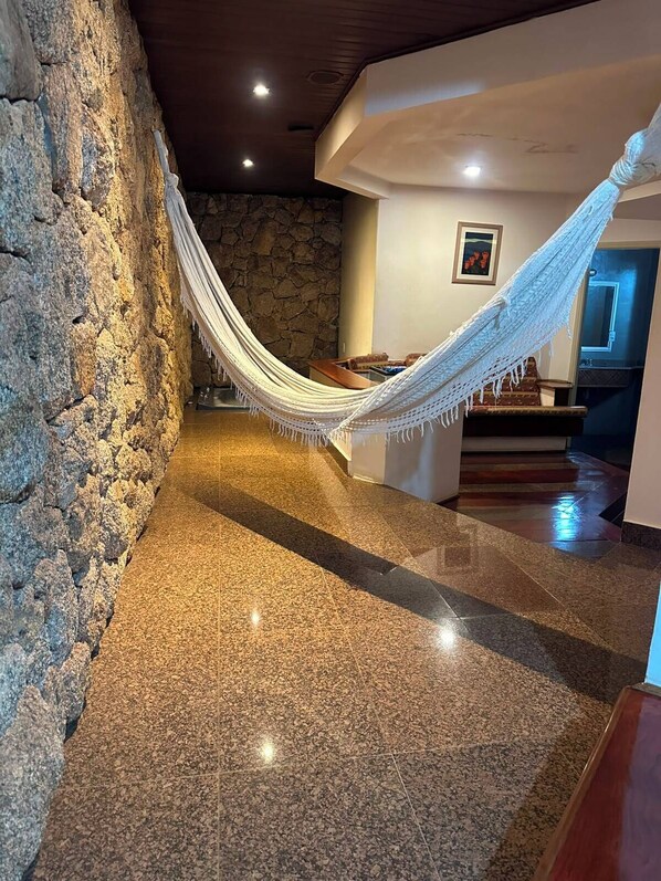 Una habitación con pared de piedra, una hamaca, una escalera de madera y suelo pulido.