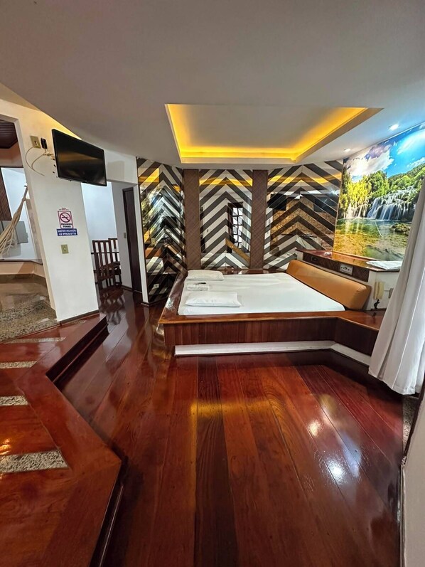 A hotel room with a bed, a TV, a desk, and a view of a waterfall. - Johnnys Motel-Hotel (Cornélio Procópio)