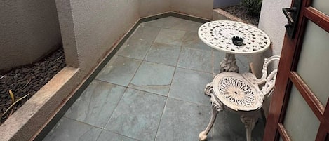 Un pequeño patio al aire libre con piso de baldosas, una mesa redonda con un tablero decorativo y una silla con patas ornamentadas.