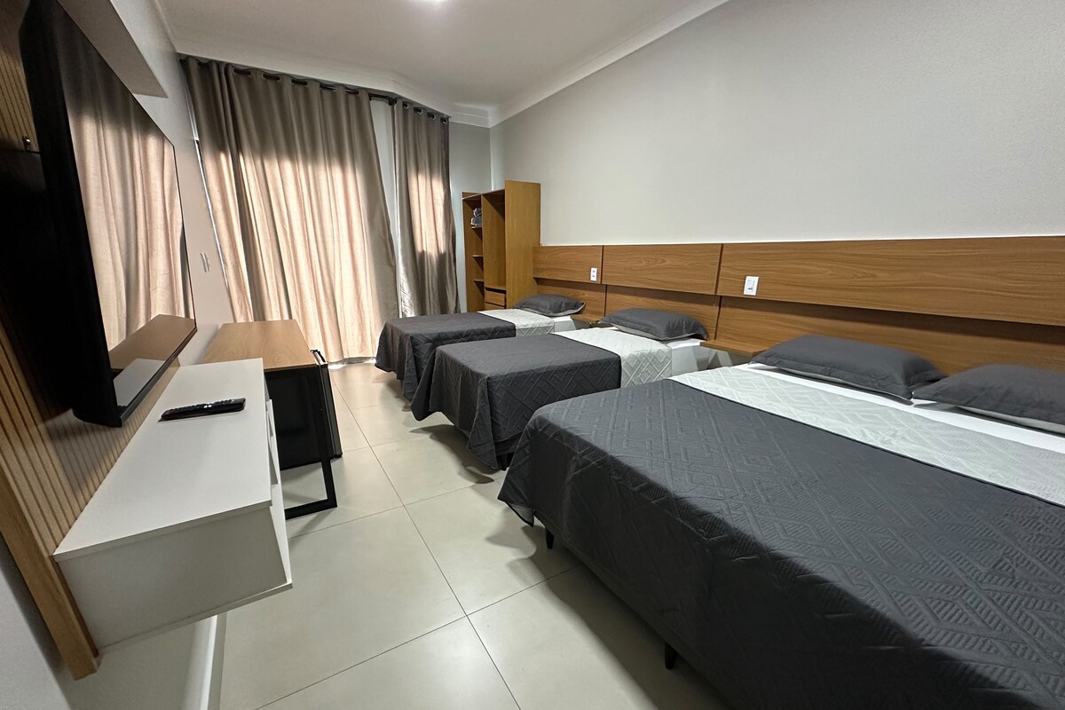 A hotel room with a bed, bedside tables, a desk, a chair, and a television.