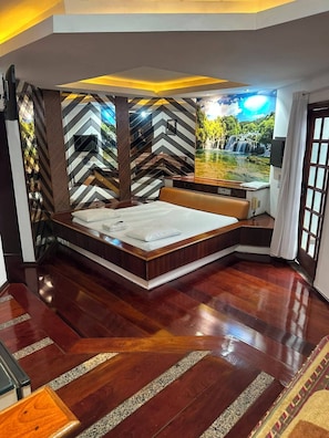 A bedroom with a large bed, a view of a waterfall, and a chevron-patterned wall.