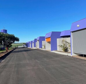 A row of single-story buildings with a flat roof, numbered sequentially, along a paved road.