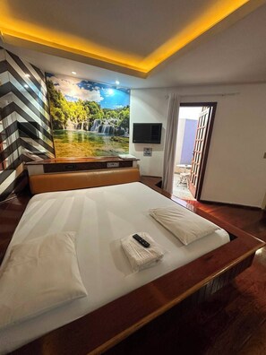 A hotel room with a large bed, a mural of a waterfall, a flat-screen TV, and a door leading to a balcony. - Johnnys Motel-Hotel (Cornélio Procópio)