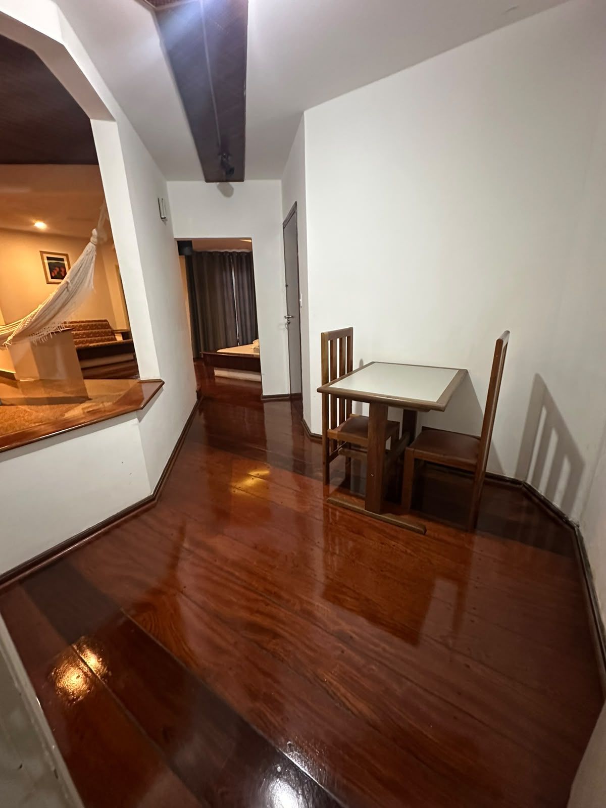 Een kamer met houten vloer, een eettafel met stoelen, een hangmat en een trap naar een ander gedeelte.