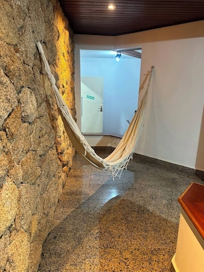 A room with a hammock against a stone wall, a door with a sign, and a wooden floor.