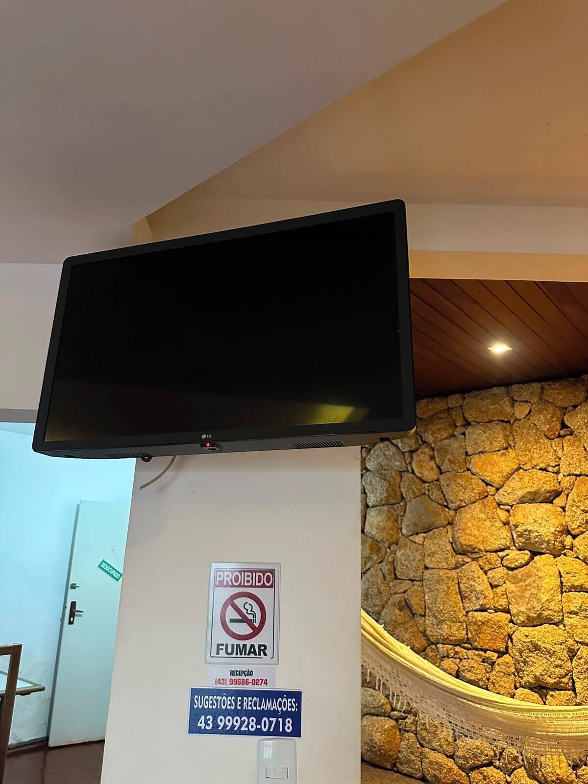 Un téléviseur à écran plat fixé au mur, avec un mur à l’aspect pierre et un plafond en bois.