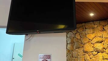 Un téléviseur à écran plat fixé au mur, avec un mur à l’aspect pierre et un plafond en bois.