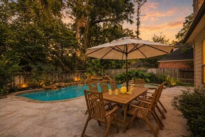 Ein Garten mit Swimmingpool, einer Holzterrasse und einem Tisch mit Stühlen unter einem großen Sonnenschirm.