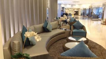 A modern hotel lobby with a curved sofa, wicker chairs, and a glass coffee table.
