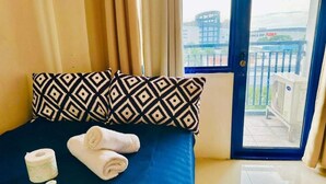 Et hotelværelse med en seng, en mønstret pude, et sammenrullet håndklæde og en toiletpapirrulle.