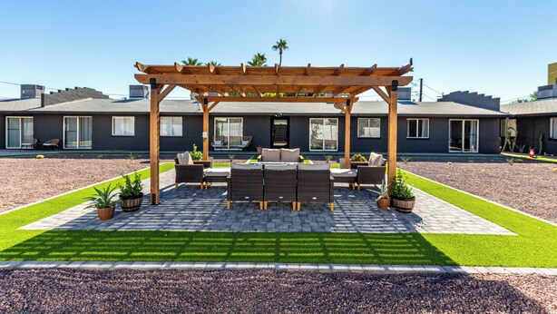 A modern house with a covered patio, outdoor furniture, and a well-maintained lawn.