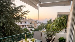 Un balcon avec une table dressée pour deux personnes, des chaises, un pot de fleurs et une vue sur le paysage urbain.