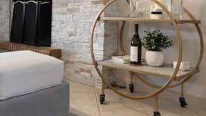 Un salon moderne avec une cheminée en pierre, un canapé gris, une étagère ronde à cadre doré agrémentée d’objets décoratifs et un téléviseur à écran plat fixé au mur.
