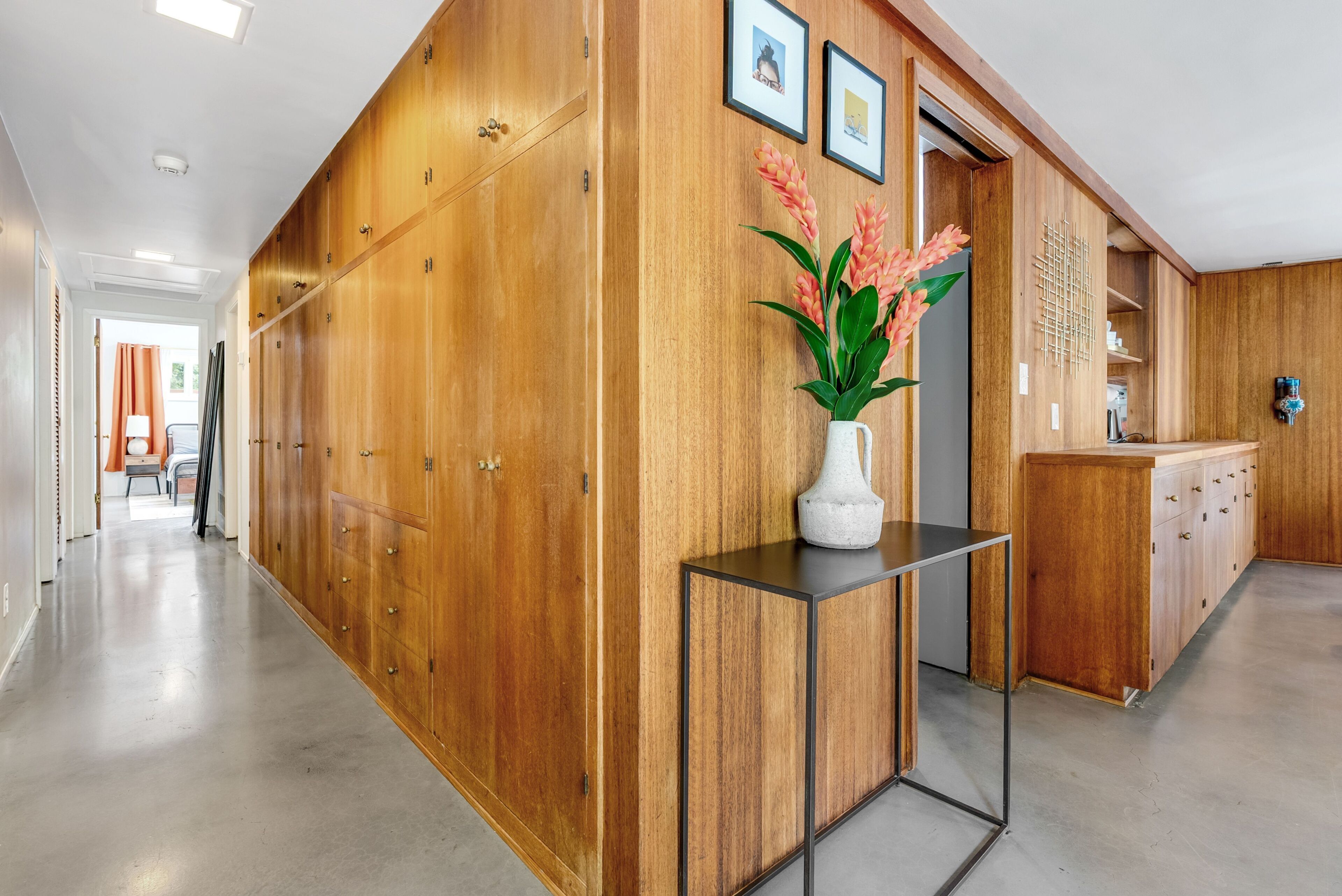 A hallway with wooden cabinets, a white vase with flowers, and a metal table.