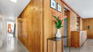 Un pasillo con armarios de madera, un jarrón blanco con flores y una mesa de metal.