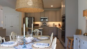 Una cucina moderna con zona pranzo, caratterizzata da un'ampia lampada intrecciata, elettrodomestici in acciaio inossidabile e colori neutri ed eleganti.