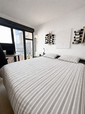 Ein Schlafzimmer mit einem großen Bett, einem Schreibtisch mit einem Laptop, einem wandmontierten Weinkühler und einem Fenster mit Blick.