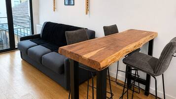 Una sala de estar moderna con una mesa de comedor de madera, taburetes de metal negro, un sofá gris y un cuadro en blanco y negro colgado en la pared.