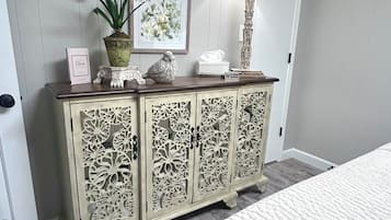 A bedroom with a bed, a cabinet with intricate carvings, a lamp, and framed artwork on the wall.