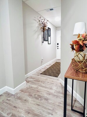 A hallway with a wooden floor, a rug, a table with a lamp, and wall-mounted decorations. - Lakeview 1BR/1BA guest suite, close to Asheville, hiking, skiing, rafting, BRP. (Weaverville)