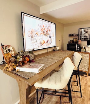 A dining area with a long table, chairs, a television mounted on the wall, and various decorative items on the table. - Lakeview 1BR/1BA guest suite, close to Asheville, hiking, skiing, rafting, BRP. (Weaverville)
