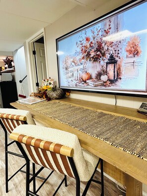 A dining area with a long wooden table, two striped chairs, and a large framed painting of a winter scene. - Lakeview 1BR/1BA guest suite, close to Asheville, hiking, skiing, rafting, BRP. (Weaverville)