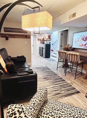 A modern living room with a black leather sofa, a leopard print ottoman, a dining area with striped chairs, and a kitchen in the background. - Lakeview 1BR/1BA guest suite, close to Asheville, hiking, skiing, rafting, BRP. (Weaverville)