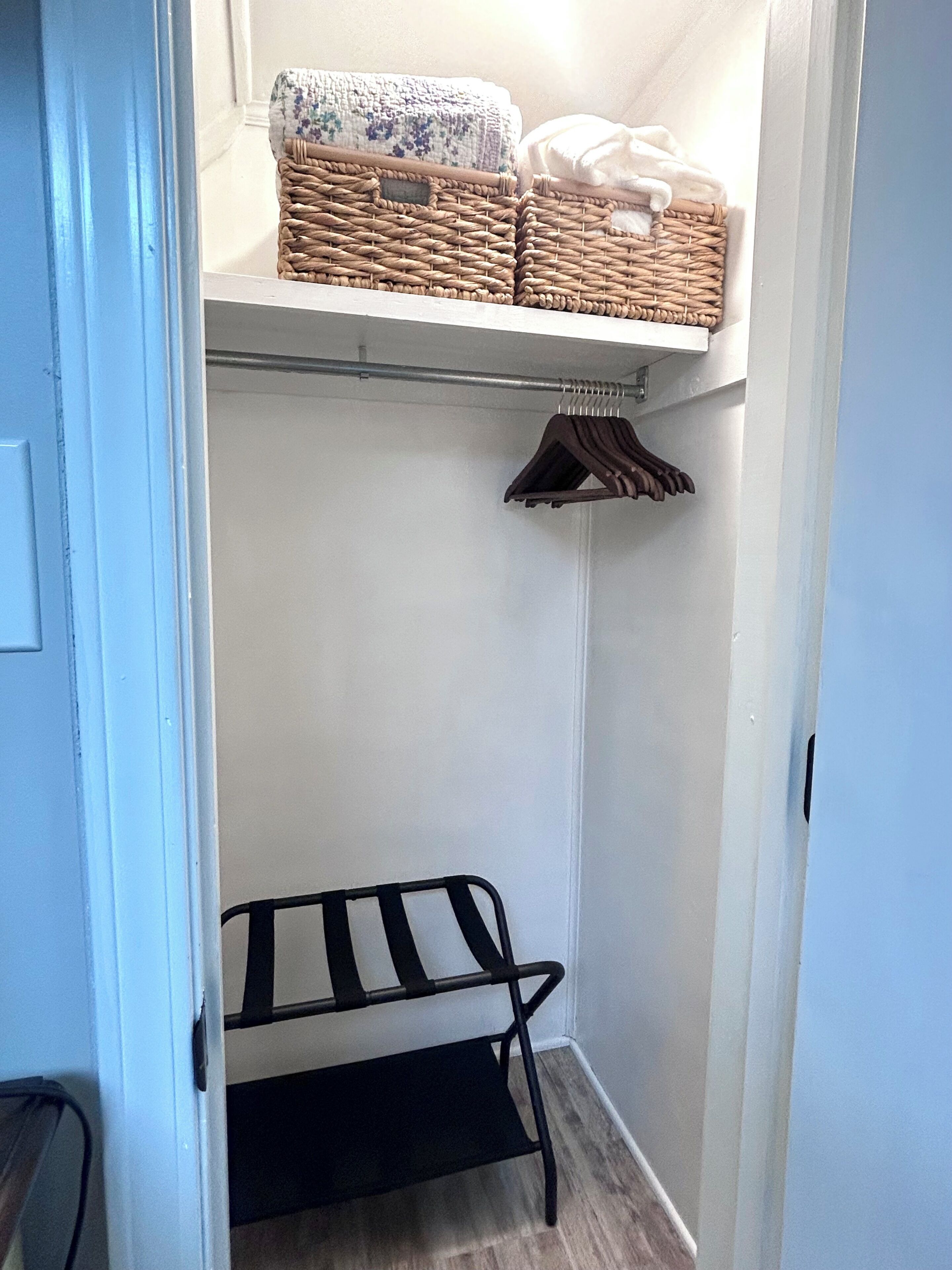 A narrow hallway with a metal bench, a hanging rack, and wicker baskets on a shelf.