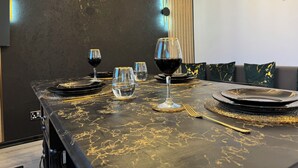 A dining table set with wine glasses, plates, and cutlery, with a dark textured wall and a modern light fixture in the background.