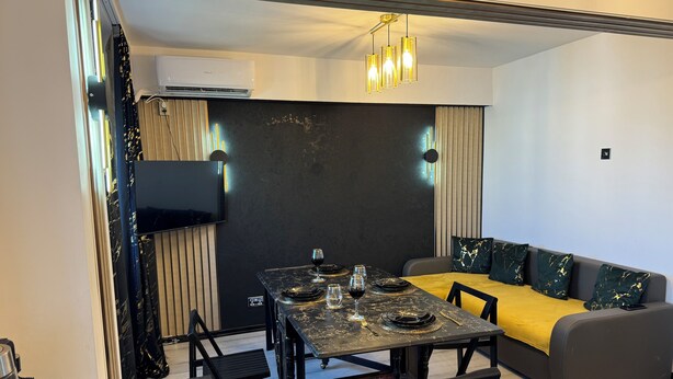 A modern dining area with a black marble table, black chairs, a yellow sofa, and a mounted flat-screen TV.