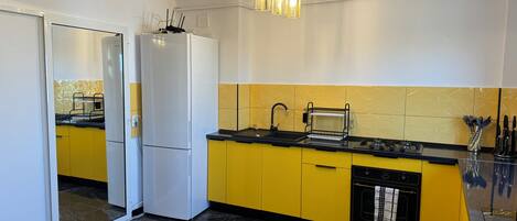 A modern kitchen with a white refrigerator, yellow cabinets, a black countertop, a sink, and a hanging light fixture.