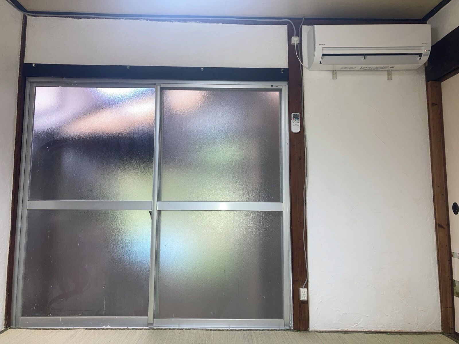 A room with a sliding glass door, a wall-mounted air conditioner, and a power outlet.
