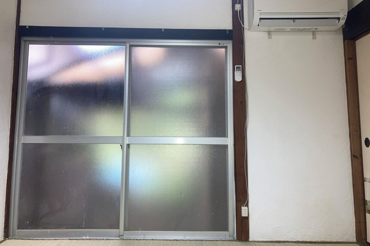 Habitación con puerta corrediza de vidrio, aire acondicionado de pared y toma de corriente.
