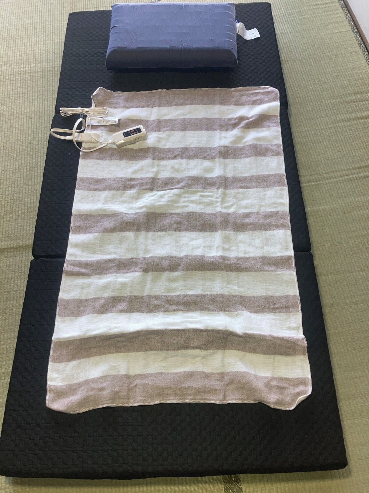 A bed with a striped blanket, a pillow, and a remote control on a black mattress.