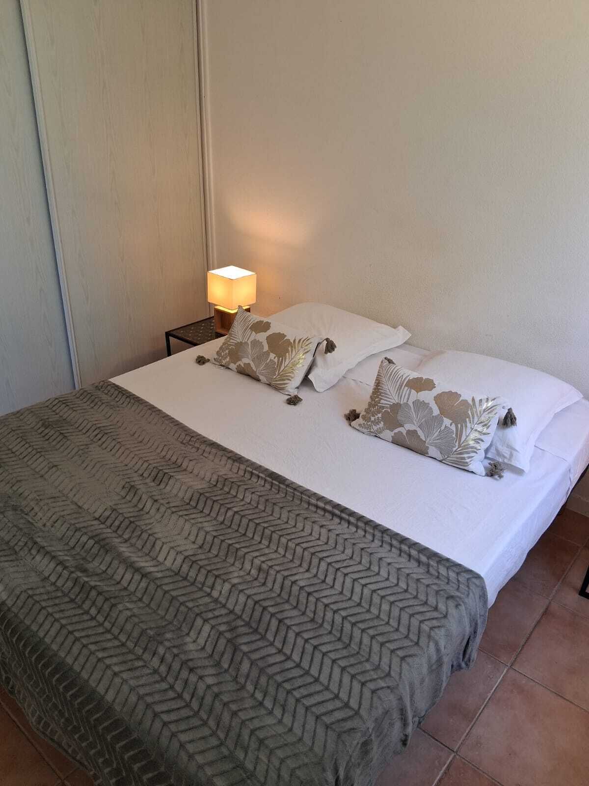 Un lit bien fait, avec une couvre-lit à motifs et des oreillers, une lampe de chevet et un mur sobre.