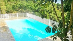 En rektangulär swimmingpool med ett vitt staket, omgiven av frodig grönska och träd.