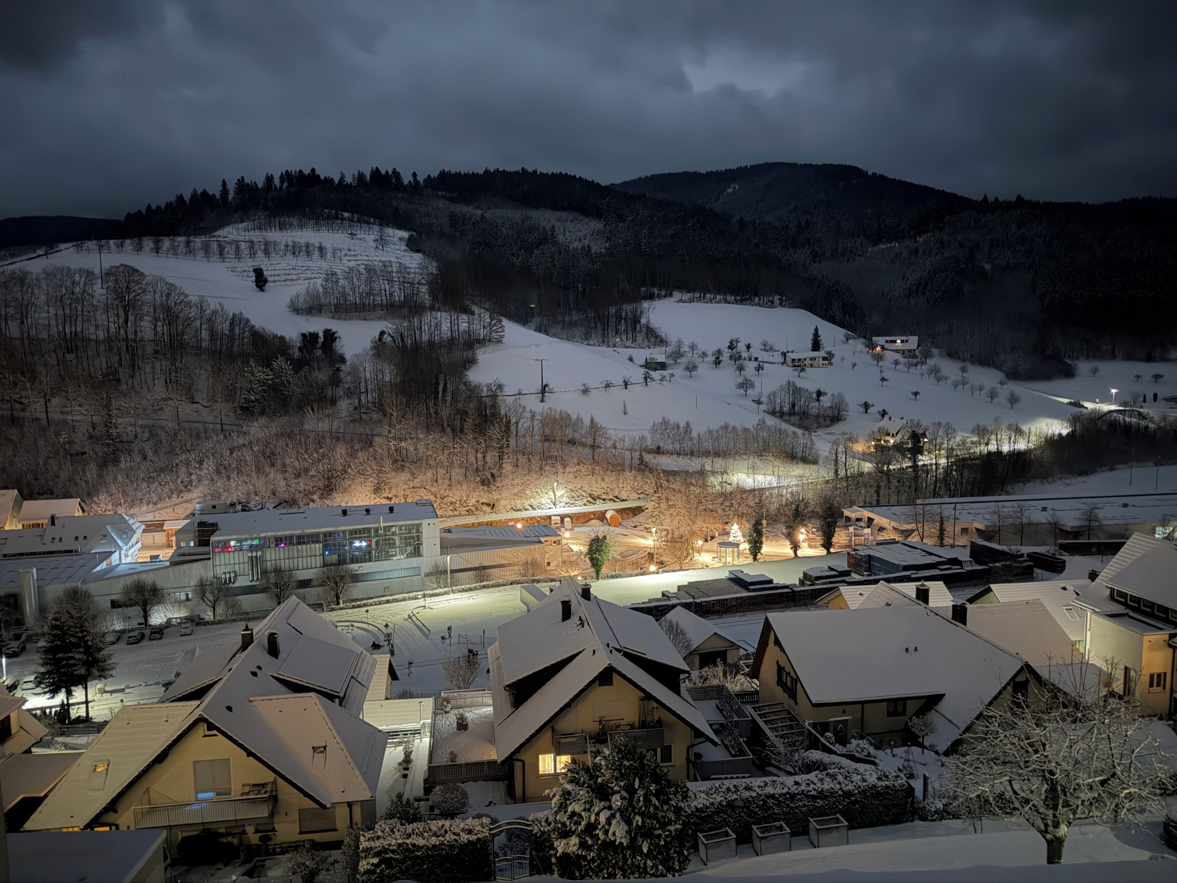 A snow-covered residential area with houses, a ski slope, and a modern building with large windows.