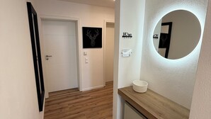 Un corridoio con pavimento in legno, una porta bianca, uno specchio fissato al muro e un quadro raffigurante un cervo impagliato.