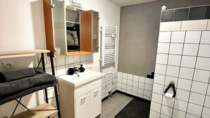 A bathroom with a white sink, mirror, and toilet, a towel rack, and a shelf with a towel. - Cosy, modern studio - Gard (Saint-Ambroix)